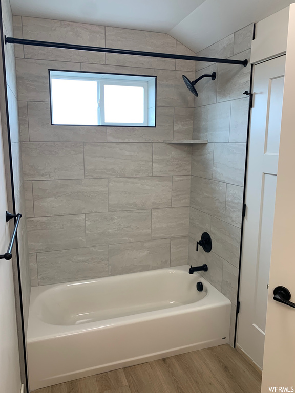 Bathroom with light hardwood flooring, tiled shower / bath combo, and lofted ceiling