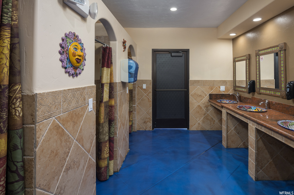 Bathroom featuring dark tile flooring, tile walls, dual large bowl vanity, and mirror