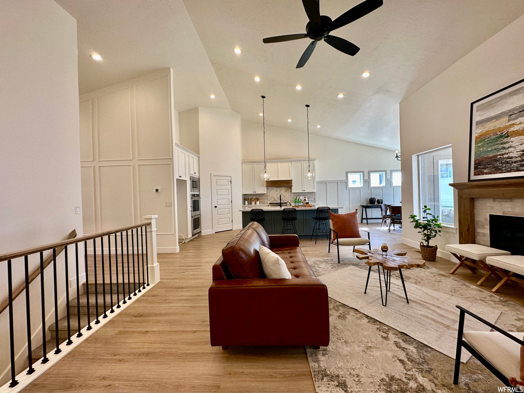 Hardwood floored living room featuring a high ceiling, vaulted ceiling, a fireplace, and ceiling fan