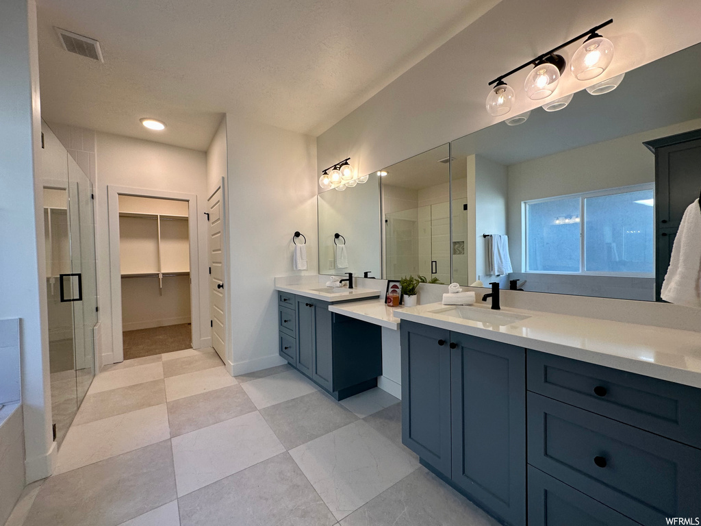 Bathroom with dual vanity, a shower with shower door, mirror, and light tile floors