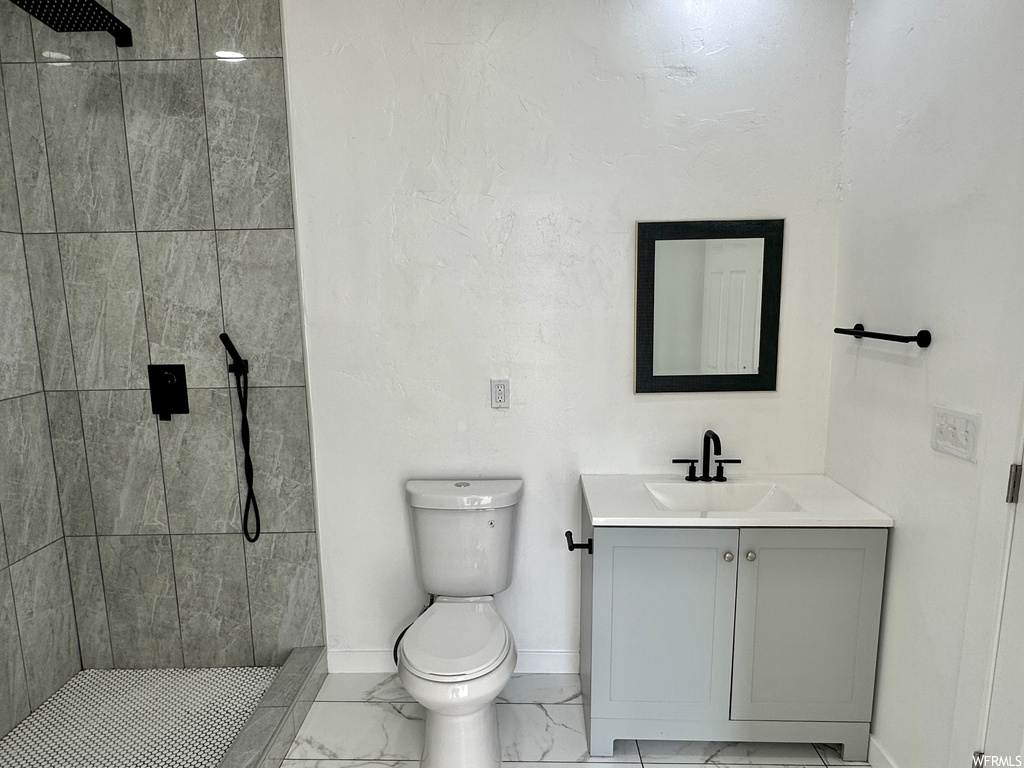 Bathroom featuring tiled shower, vanity with extensive cabinet space, mirror, and light tile floors
