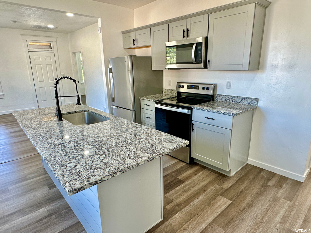 Kitchen featuring appliances with stainless steel finishes, light hardwood floors, and light stone countertops