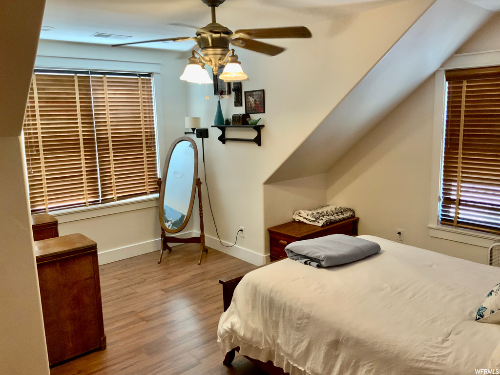 Hardwood floored bedroom with ceiling fan and lofted ceiling