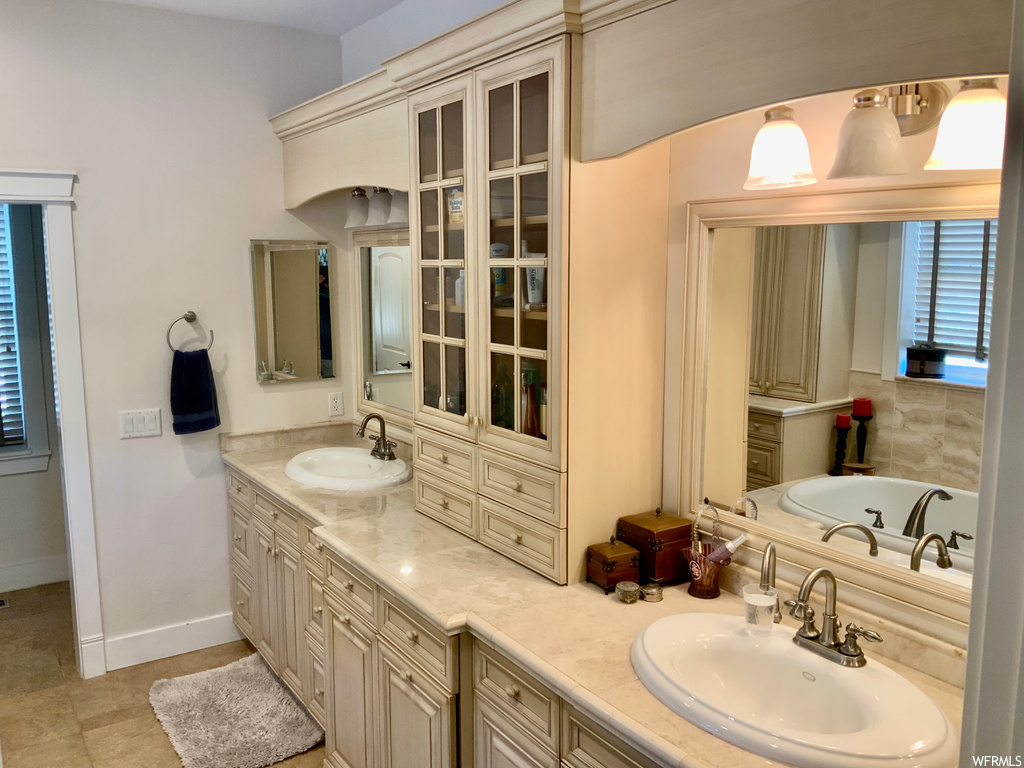 Bathroom with dual vanity, mirror, a bath, and light tile flooring