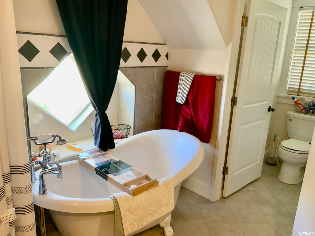 Bathroom featuring a tub, tile walls, lofted ceiling, and light tile floors