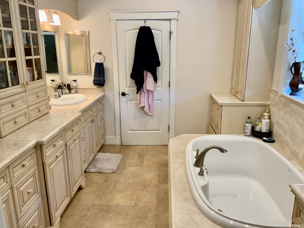 Bathroom featuring light tile floors, mirror, tiled bath, and vanity