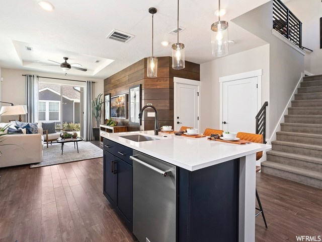 Kitchen with stainless steel dishwasher, a tray ceiling, dark hardwood floors, light countertops, hanging light fixtures, dark brown cabinets, and ceiling fan