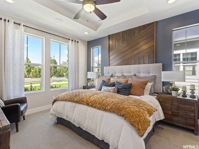 Bedroom with light carpet, ceiling fan, and a raised ceiling