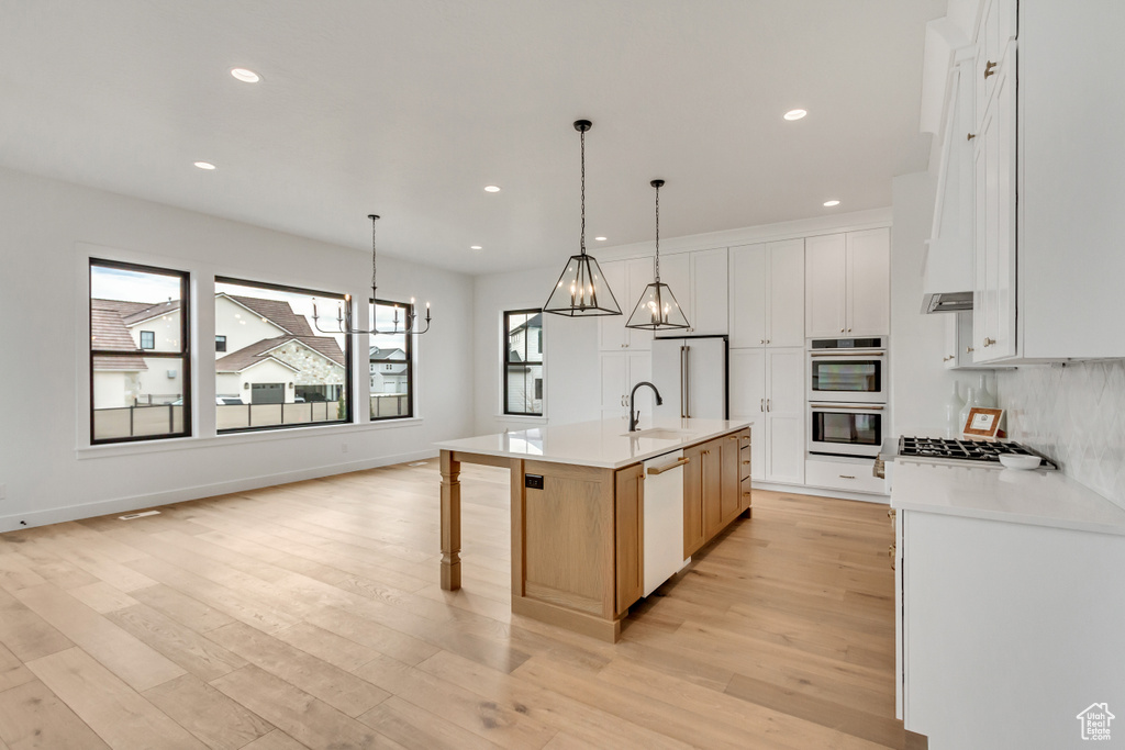 Kitchen featuring white cabinets, light hardwood / wood-style floors, hanging light fixtures, and a center island with sink