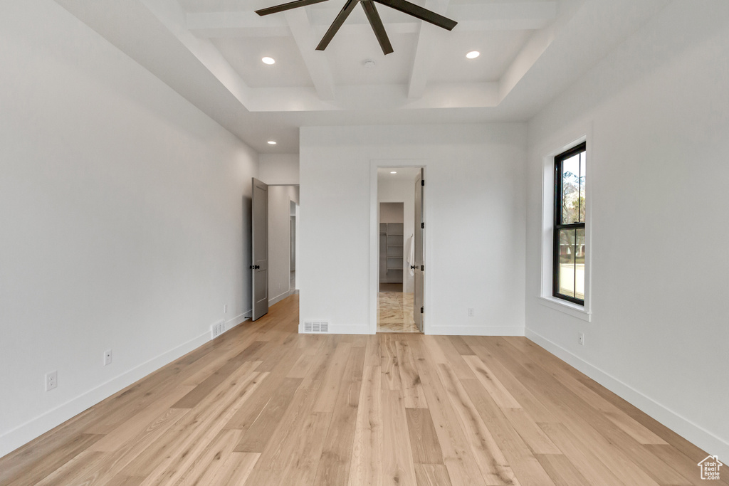 Unfurnished bedroom with a walk in closet, ceiling fan, light hardwood / wood-style floors, and beamed ceiling