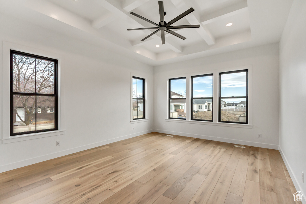 Empty room featuring coffered ceiling, light wood-type flooring, ceiling fan, and plenty of natural light