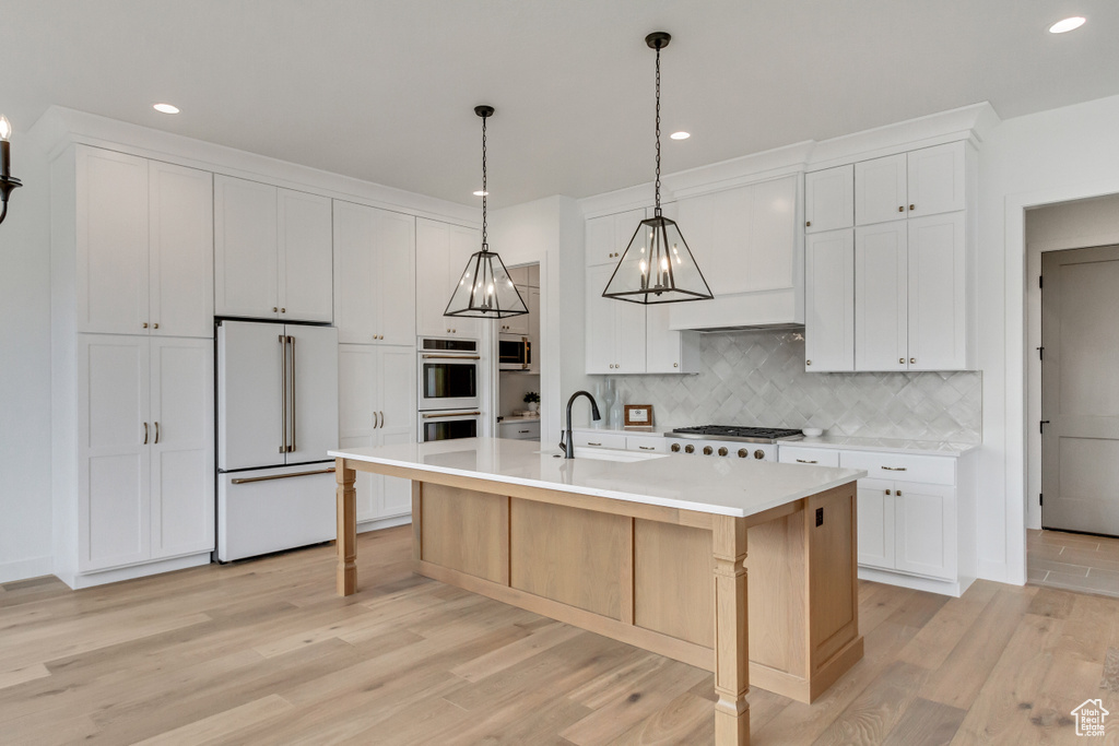Kitchen featuring appliances with stainless steel finishes, an island with sink, hanging light fixtures, and light hardwood / wood-style flooring