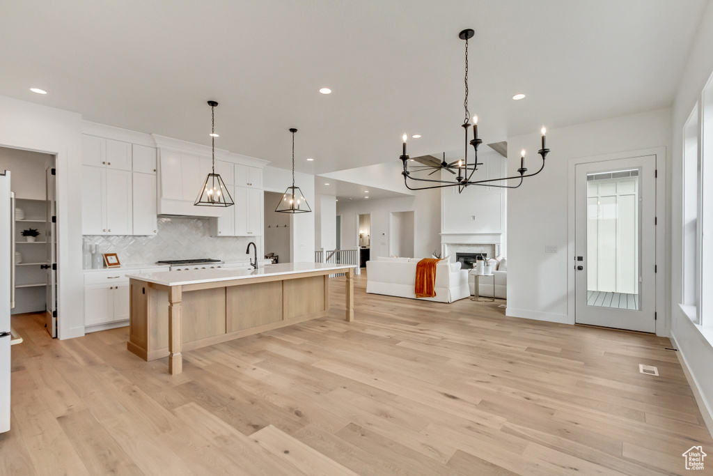Kitchen featuring white cabinets, pendant lighting, light wood-type flooring, and a center island with sink