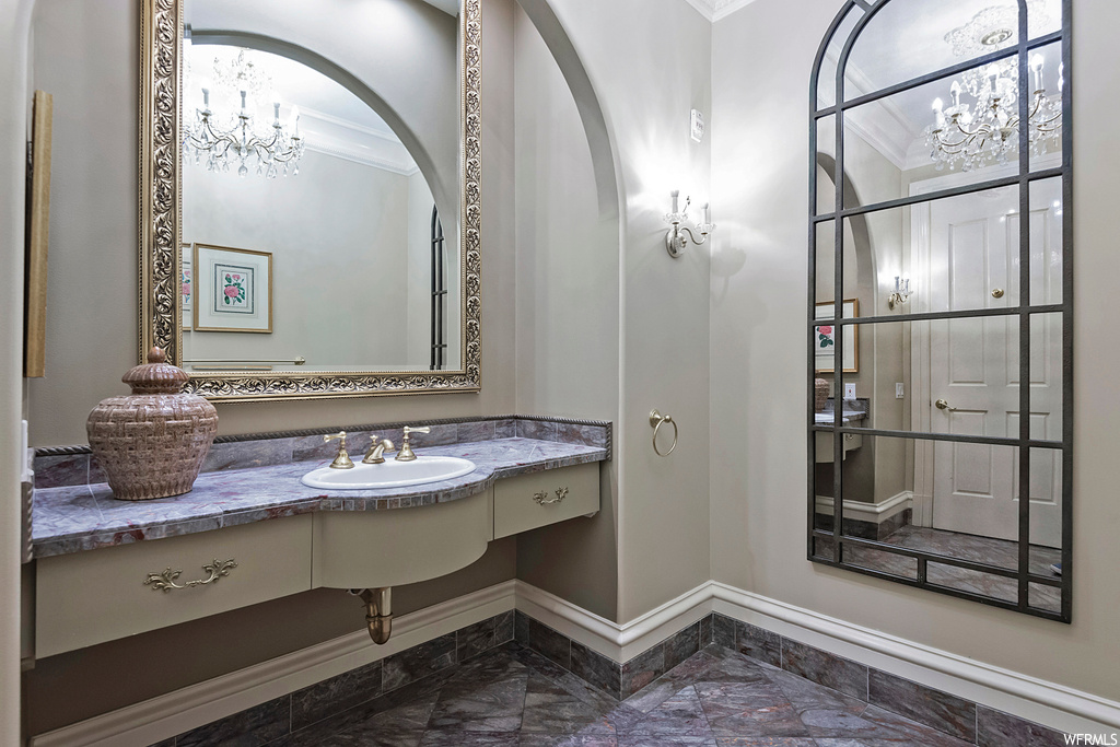 Bathroom with dark tile floors, ornamental molding, mirror, and vanity