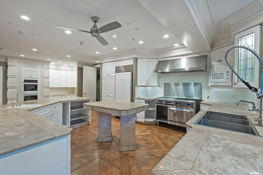 Kitchen with parquet floors, wall chimney range hood, white cabinetry, built in appliances, light stone countertops, and backsplash