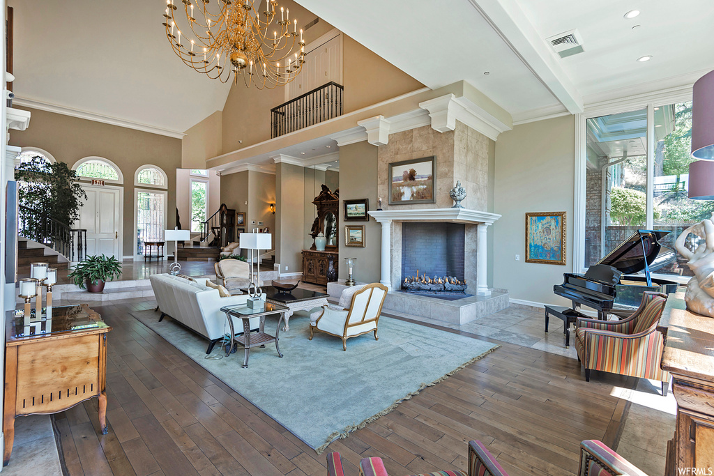 Living room with a chandelier, light hardwood flooring, vaulted ceiling with beams, a fireplace, and a high ceiling