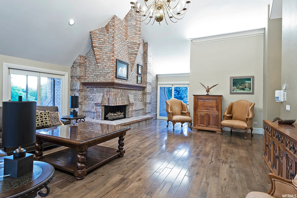 Living room with vaulted ceiling, brick wall, light hardwood flooring, a fireplace, and a high ceiling