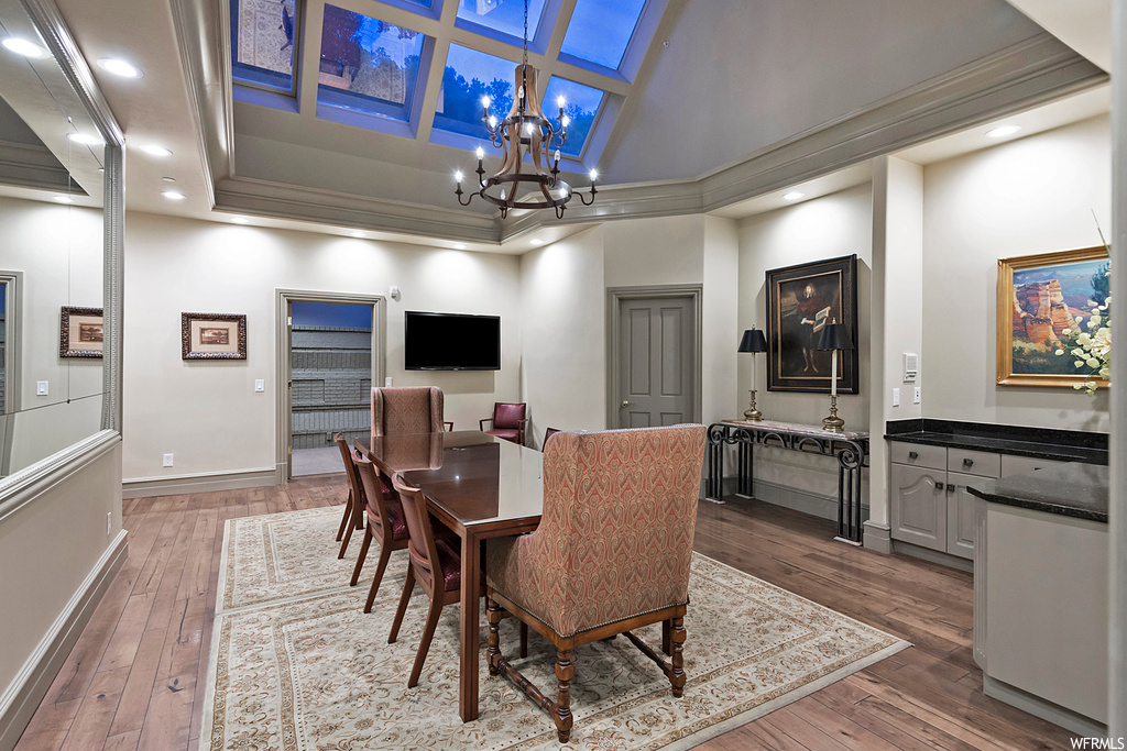 Dining room featuring a chandelier, light hardwood floors, coffered ceiling, crown molding, a raised ceiling, and a high ceiling