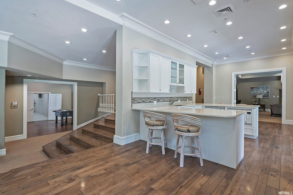 Kitchen featuring a center island, crown molding, white cabinets, dark hardwood flooring, light countertops, and backsplash