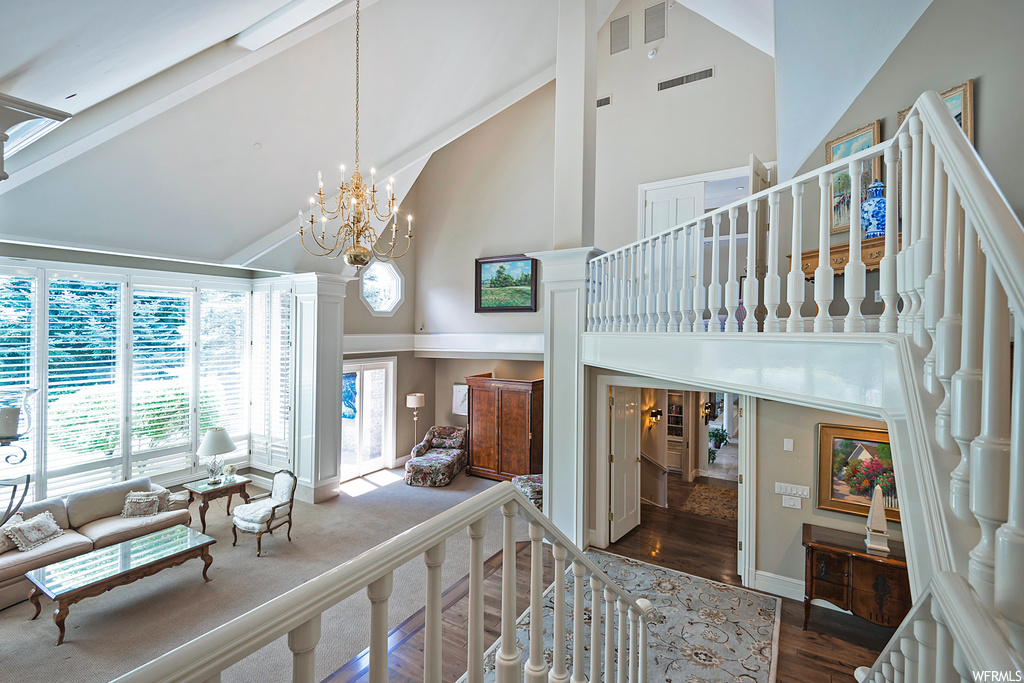 Staircase featuring a notable chandelier, a high ceiling, hardwood floors, and lofted ceiling