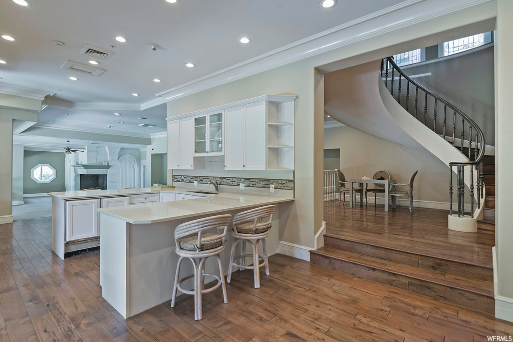 Kitchen with ornamental molding, backsplash, white cabinets, light countertops, a kitchen island, and dark hardwood flooring