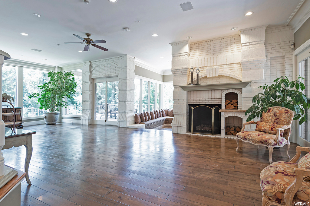 Living room with ornamental molding, brick wall, light hardwood flooring, ceiling fan, and a fireplace