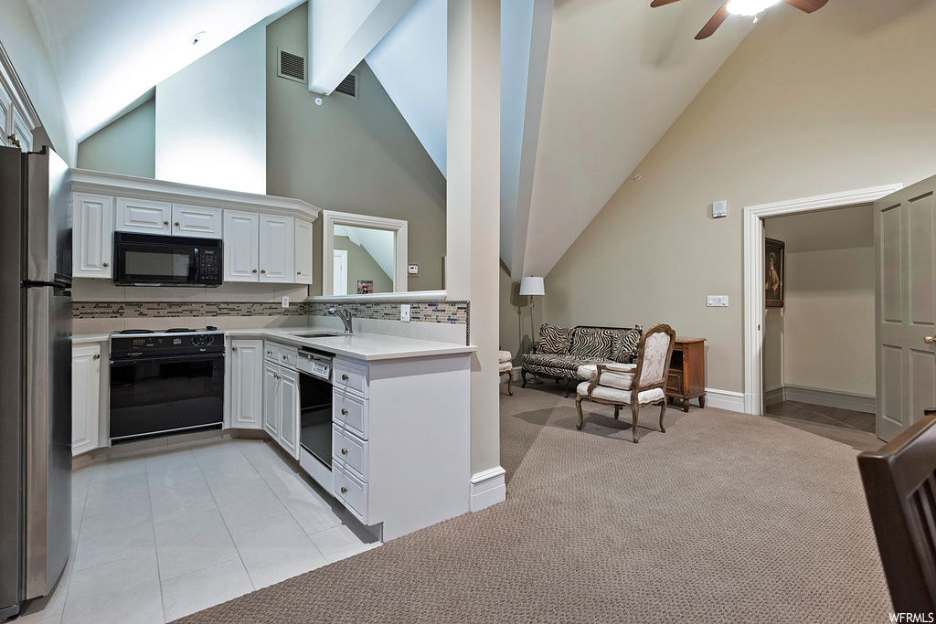 Kitchen featuring black appliances, white cabinets, lofted ceiling, light carpet, light countertops, and a high ceiling