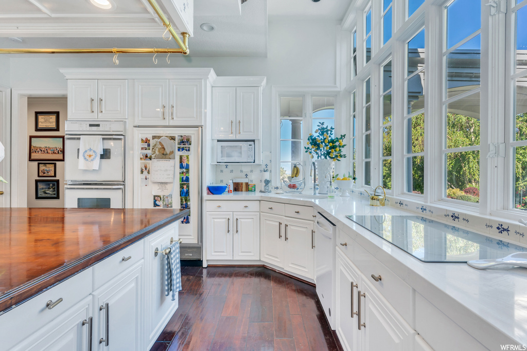 Kitchen featuring white appliances, dark hardwood floors, and white cabinetry