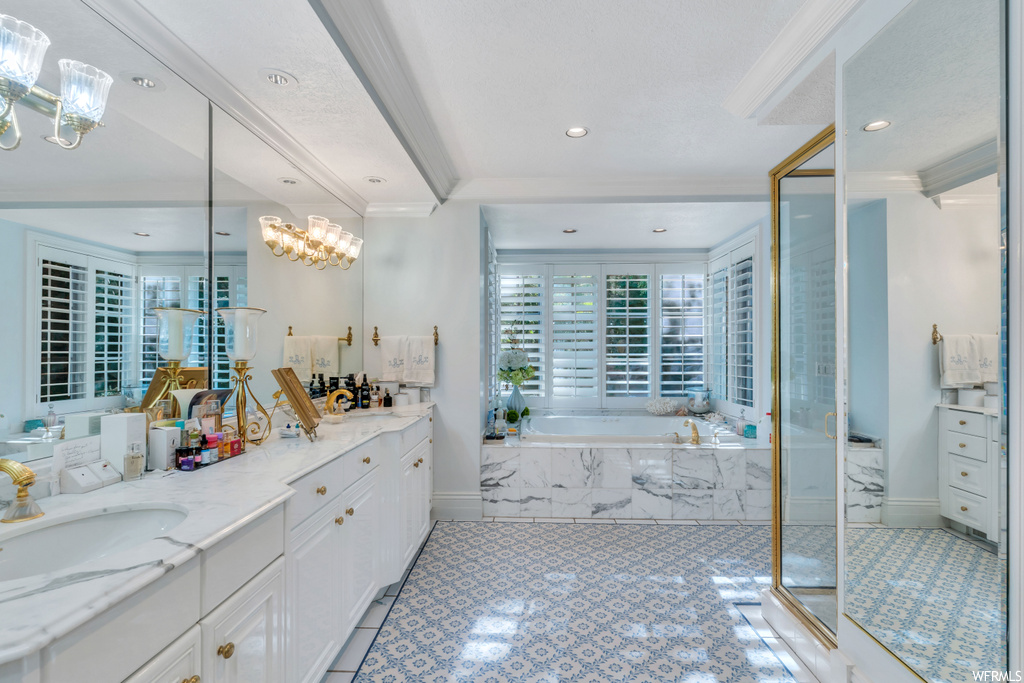 Bathroom with ornamental molding, mirror, a chandelier, separate shower and tub enclosures, light tile floors, and vanity
