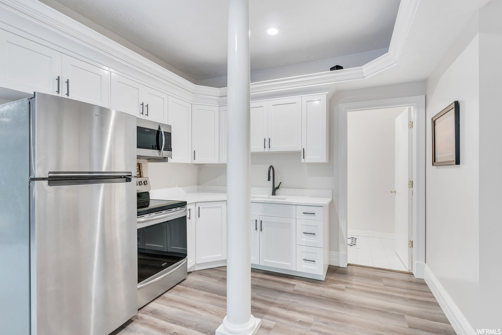 Kitchen featuring appliances with stainless steel finishes, white cabinetry, light countertops, light hardwood flooring, ornamental molding, and a raised ceiling