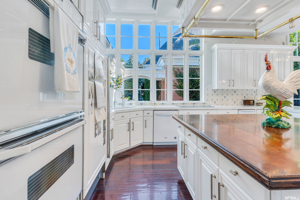 Kitchen featuring white cabinetry, dark hardwood flooring, light countertops, white appliances, ornamental molding, and backsplash