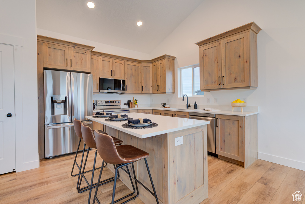Kitchen with a kitchen breakfast bar, vaulted ceiling, appliances with stainless steel finishes, light hardwood / wood-style flooring, and a center island