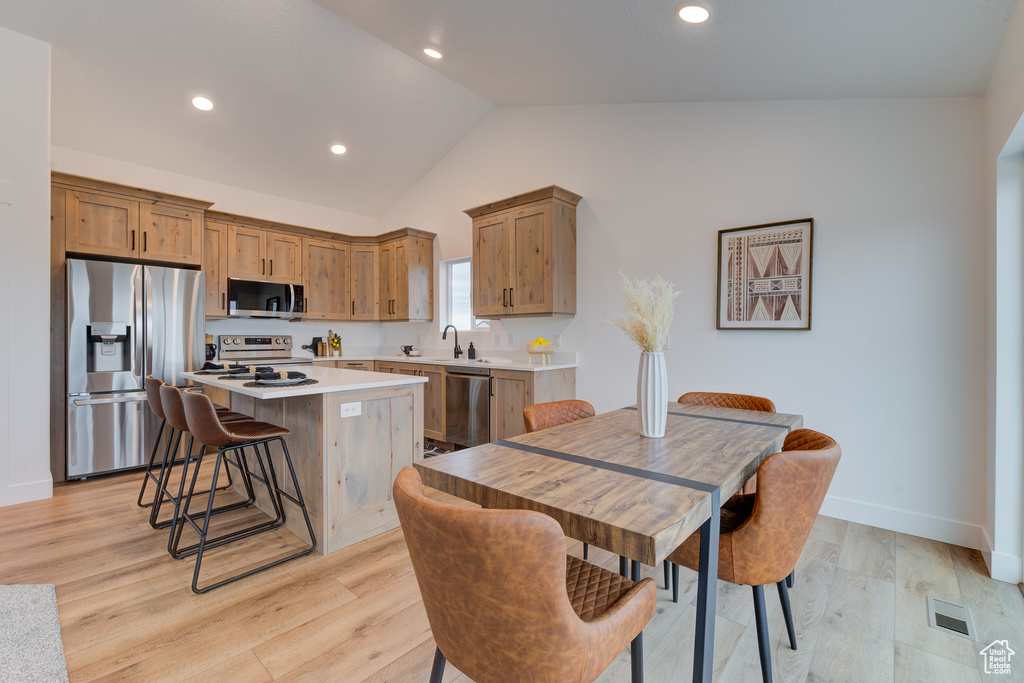 Kitchen featuring a center island, light hardwood / wood-style flooring, appliances with stainless steel finishes, and a kitchen bar