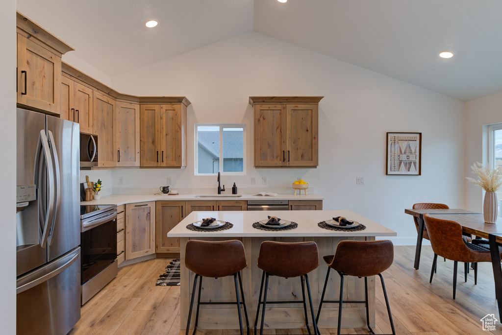 Kitchen with light hardwood / wood-style floors, a center island, stainless steel appliances, sink, and vaulted ceiling