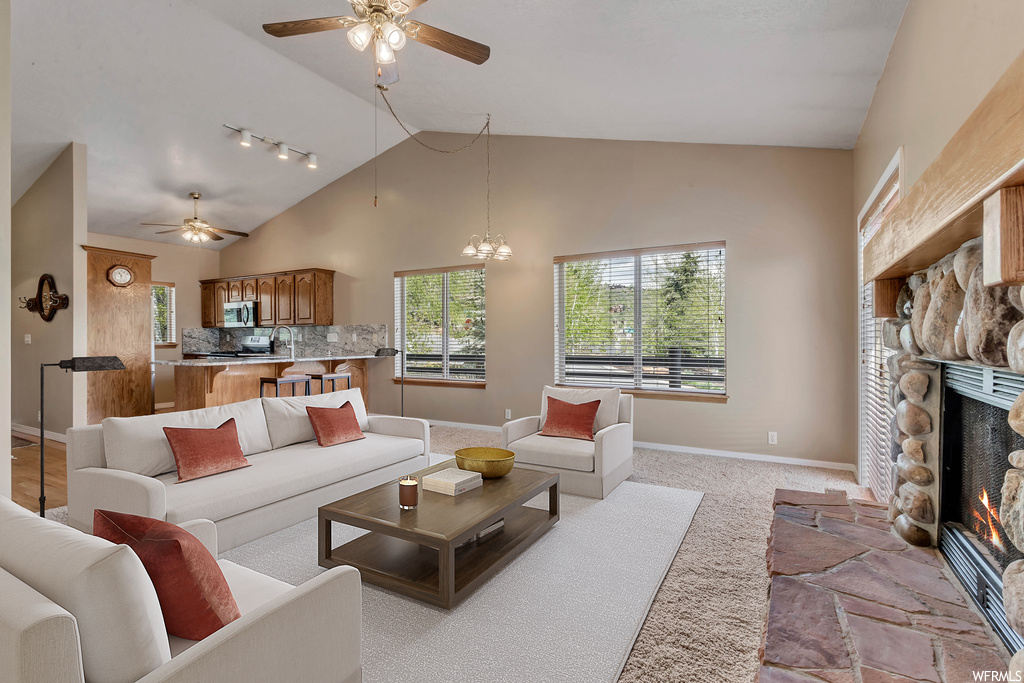 Carpeted living room featuring ceiling fan, rail lighting, a fireplace, and lofted ceiling