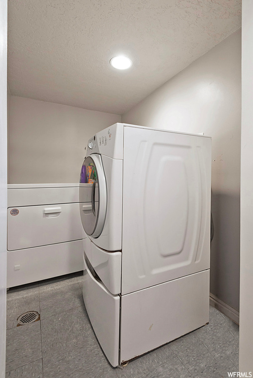 Clothes washing area with independent washer and dryer, a textured ceiling, and light tile floors