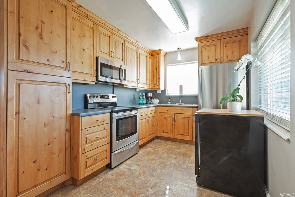 Kitchen featuring appliances with stainless steel finishes, light countertops, brown cabinets, and light tile floors