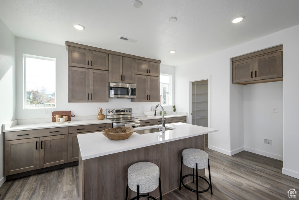 Kitchen with a kitchen island with sink, a kitchen bar, dark hardwood / wood-style flooring, sink, and stainless steel appliances