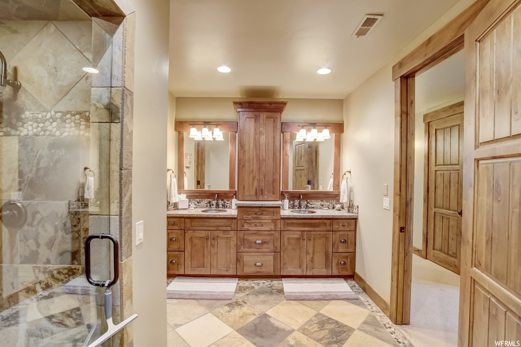 Bathroom featuring an enclosed shower, dual bowl vanity, mirror, and light tile floors