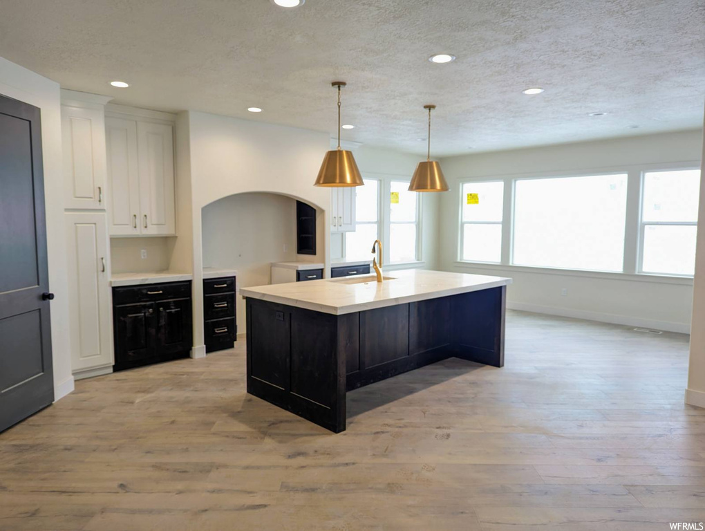 Kitchen with pendant lighting, an island with sink, light hardwood / wood-style flooring, and white cabinetry