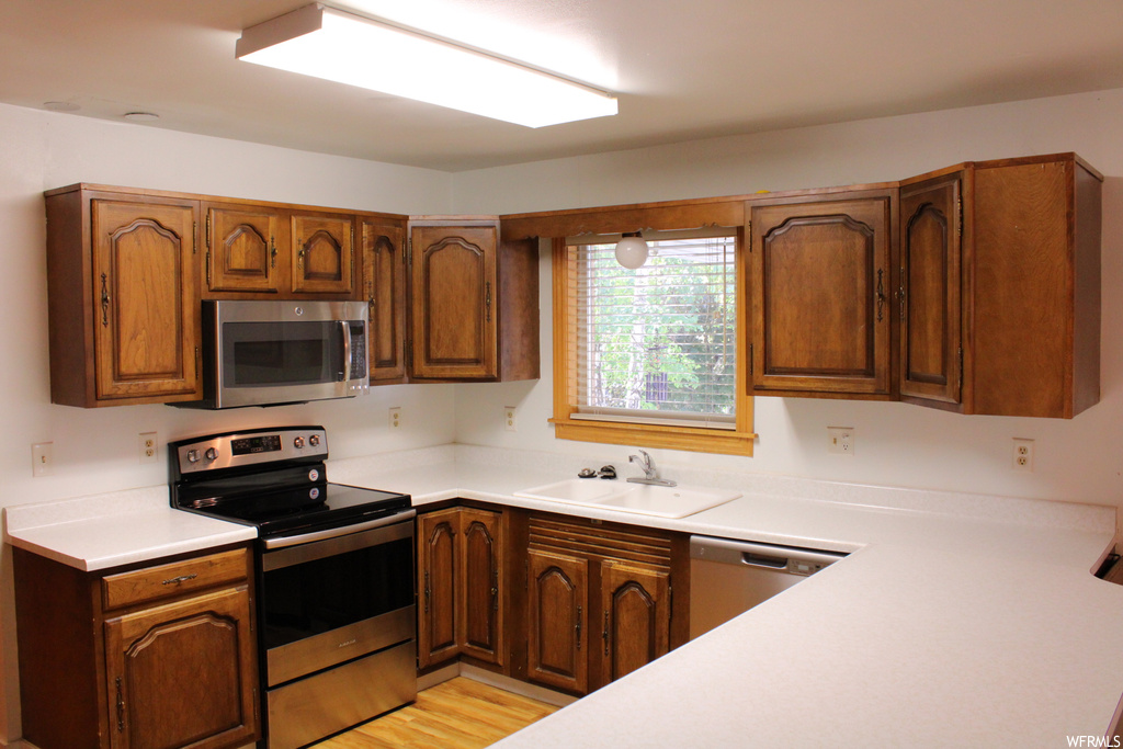 Kitchen with appliances with stainless steel finishes, brown cabinets, light countertops, and light hardwood flooring