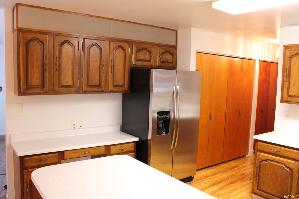 Kitchen featuring stainless steel fridge with ice dispenser, brown cabinets, light countertops, and light hardwood flooring