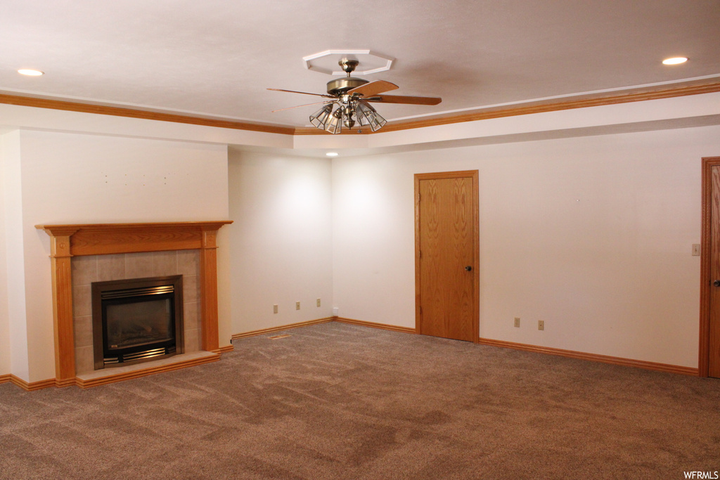 Carpeted living room featuring crown molding, ceiling fan, a fireplace, and a raised ceiling