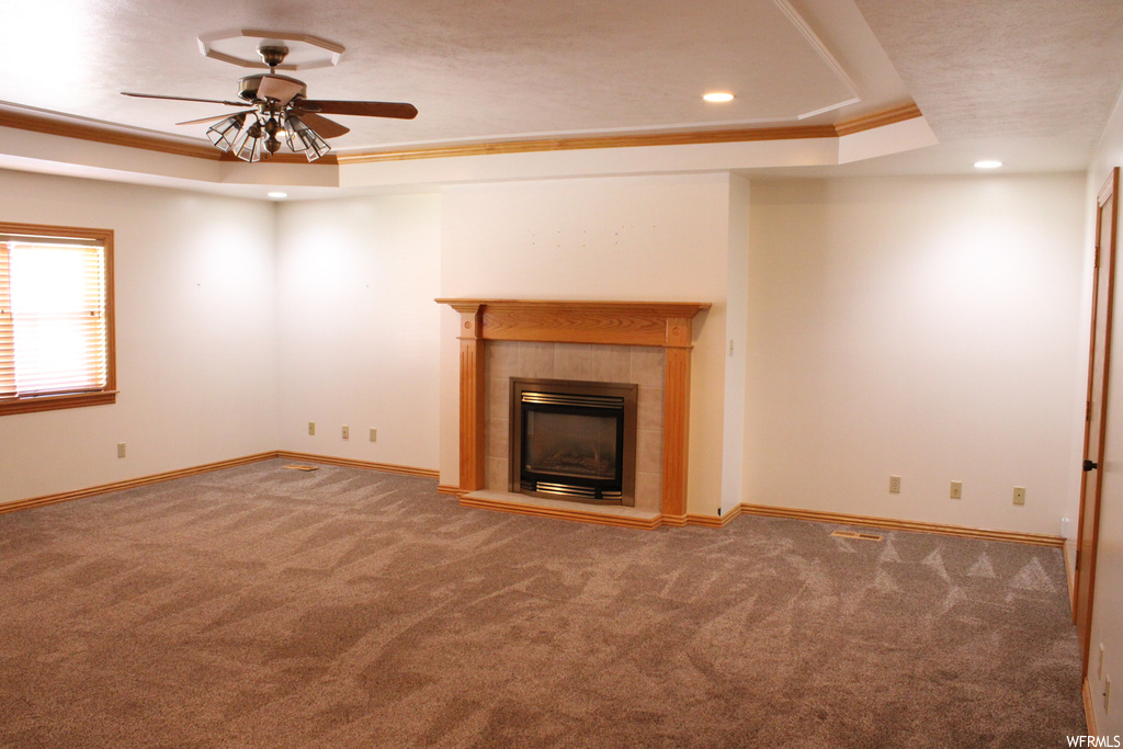 Carpeted living room featuring ceiling fan, a tray ceiling, a fireplace, and crown molding