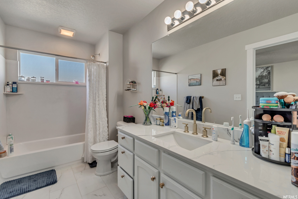 Full bathroom with a textured ceiling, mirror, light tile floors, shower / bath combo with shower curtain, and large vanity