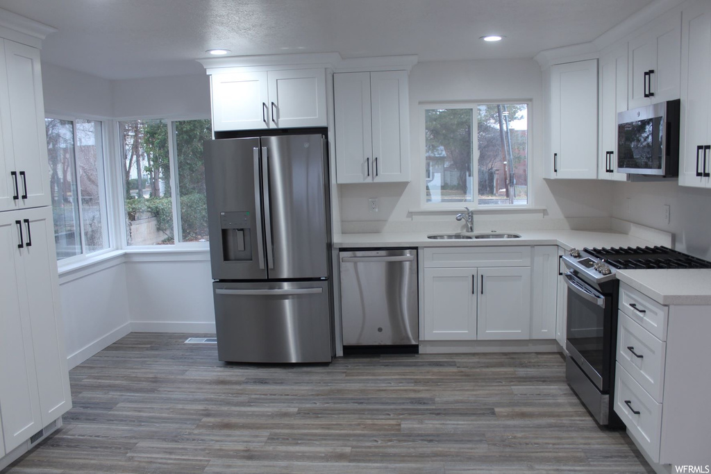 Kitchen with light countertops, appliances with stainless steel finishes, white cabinets, and light hardwood flooring