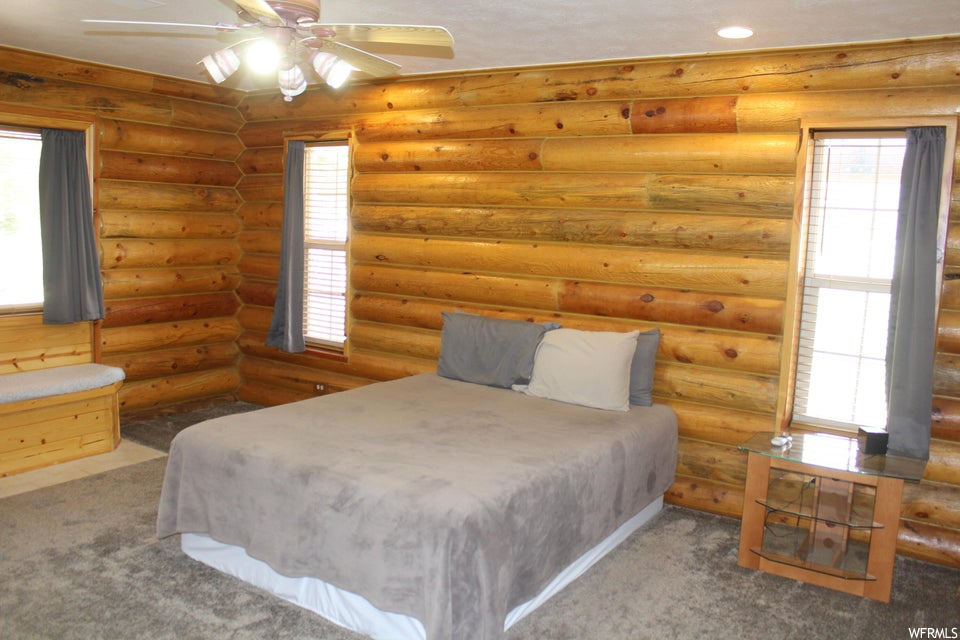 Bedroom with ceiling fan, log walls, and carpet flooring