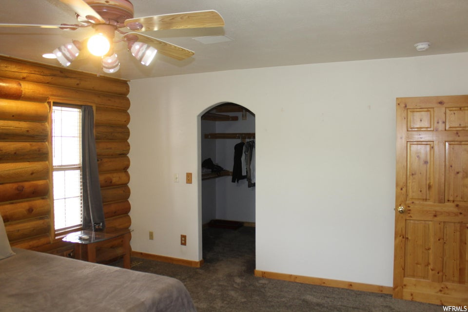 Carpeted bedroom featuring multiple windows, log walls, and ceiling fan