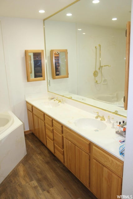 Bathroom with a washtub, wood-type flooring, double sink vanity, and mirror