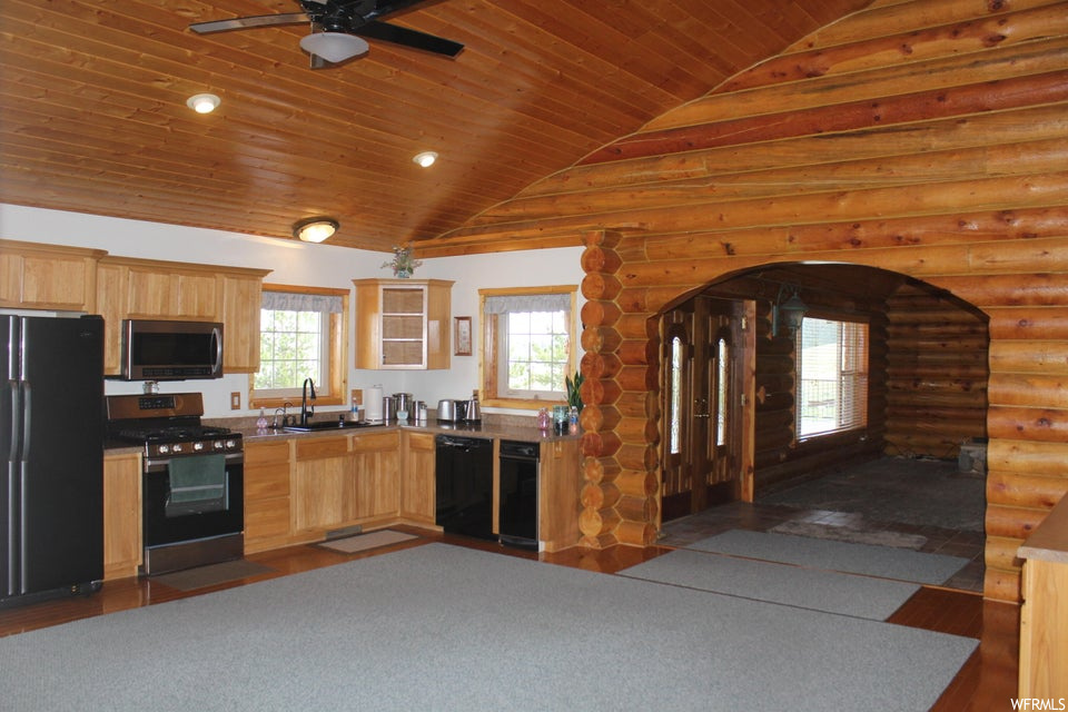 Kitchen with log walls, vaulted ceiling, black appliances, wooden ceiling, hardwood flooring, ceiling fan, dark countertops, and a high ceiling